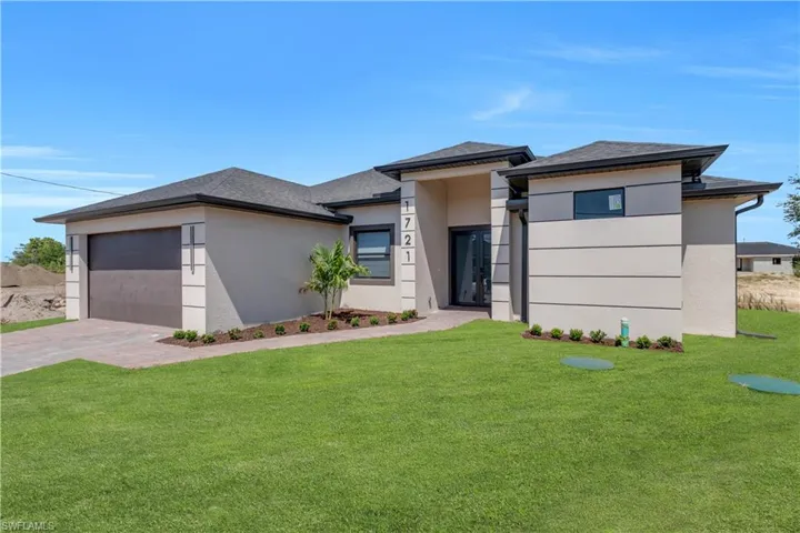 Prairie-style home with a front lawn, an attached garage, stucco siding, driveway, and roof with shingles