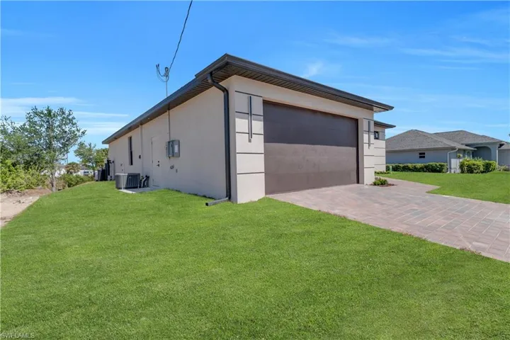 View of side of property featuring decorative driveway, a garage, a yard, and stucco siding