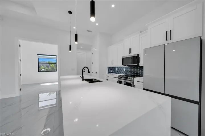 Kitchen featuring appliances with stainless steel finishes, white cabinets, light stone countertops, an island with sink, and recessed lighting