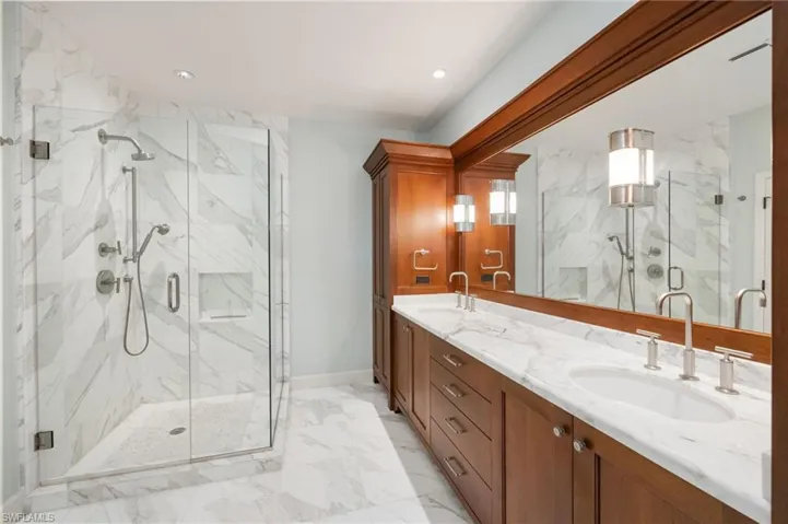 Bathroom with double vanity, a marble finish shower, and light marble finish floors
