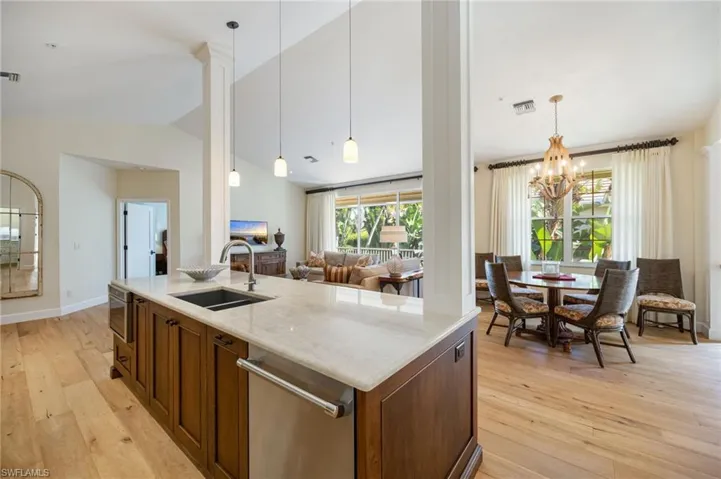 Kitchen featuring decorative light fixtures, light wood-style floors, vaulted ceiling, light stone countertops, and appliances with stainless steel finishes