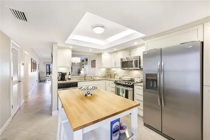 Kitchen with a raised ceiling, wooden counters, backsplash, white cabinetry, and stainless steel appliances