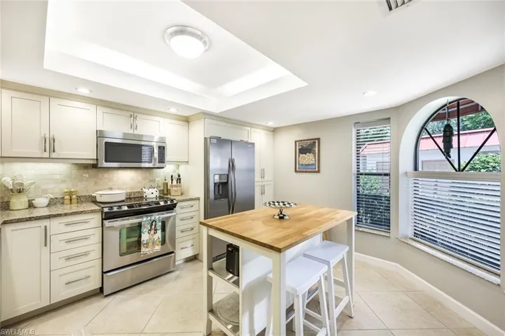 Kitchen with light tile patterned flooring, appliances with stainless steel finishes, light stone counters, tasteful backsplash, and a raised ceiling