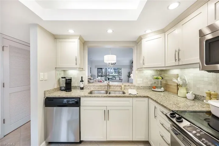 Kitchen featuring backsplash, appliances with stainless steel finishes, light stone counters, light tile patterned floors, and sink