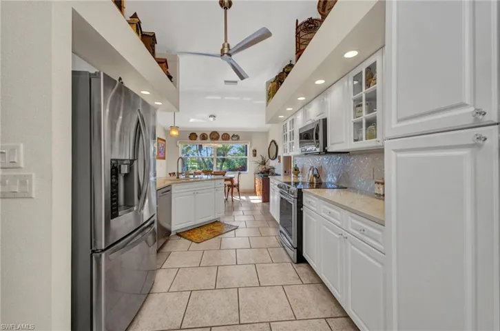Kitchen with stainless steel appliances, decorative backsplash, white cabinetry, glass insert cabinets, and recessed lighting