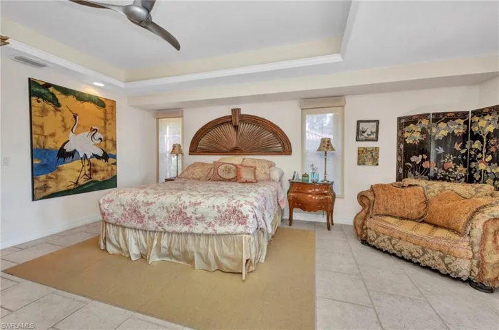 Bedroom featuring light tile patterned floors, multiple windows, a raised ceiling, and ceiling fan
