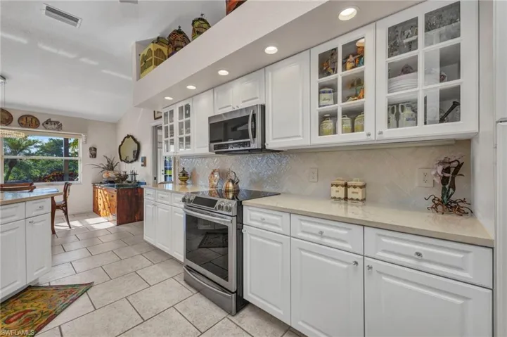Kitchen with stainless steel appliances, backsplash, white cabinets, glass insert cabinets, and recessed lighting