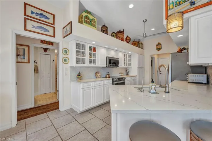 Kitchen featuring stainless steel appliances, a peninsula, white cabinetry, tasteful backsplash, and glass insert cabinets