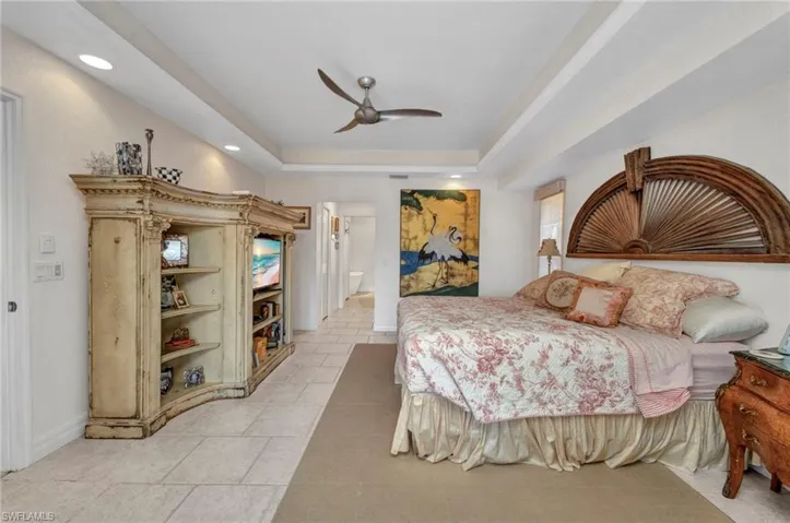 Bedroom with light tile patterned flooring, a tray ceiling, recessed lighting, ceiling fan, and connected bathroom
