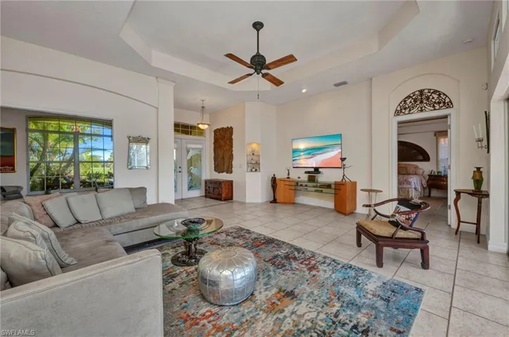 Living room featuring ceiling fan, a tray ceiling, and light tile patterned floors