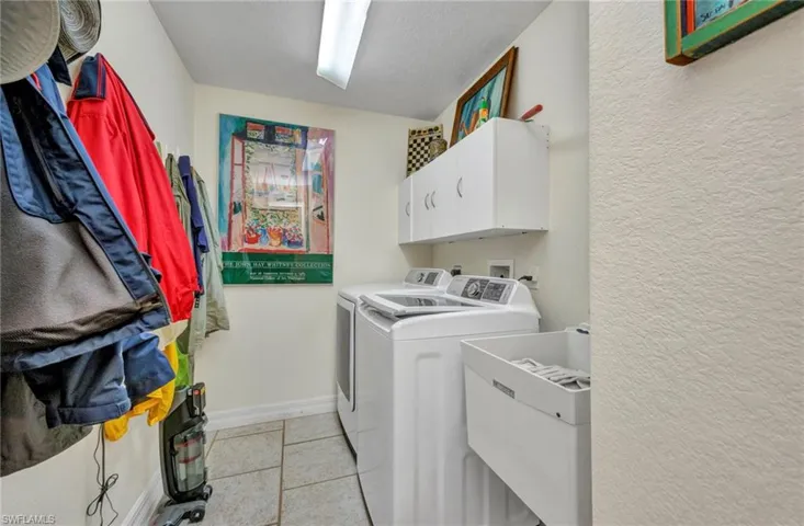 Washroom featuring independent washer and dryer, cabinet space, light tile patterned floors, and a textured wall