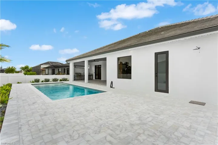 Expansive pool area with white marble and access to a Pool Cabana Bathroom and outdoor shower/ducha.