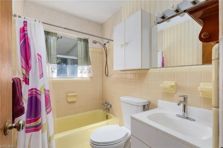 Bathroom with vanity, shower / bath combo with shower curtain, tile walls, and backsplash