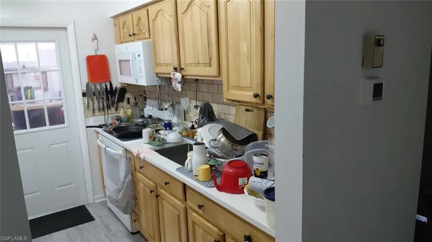 Kitchen featuring white microwave, decorative backsplash, light countertops, light brown cabinetry, and light wood finished floors