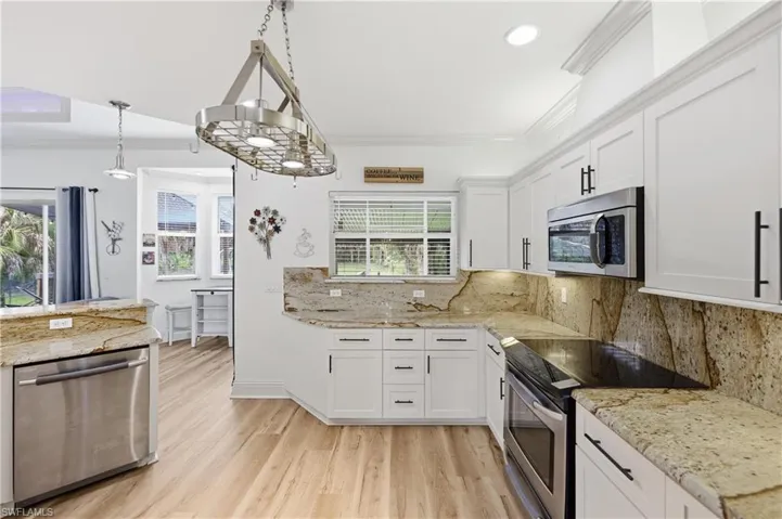Spacious kitchen featuring white cabinetry, granite countertops, stainless steel appliances, and an open layout to the living areas.