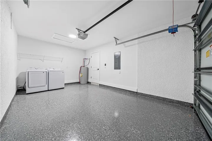 Garage featuring a textured wall, water heater, electric panel, and washing machine and clothes dryer