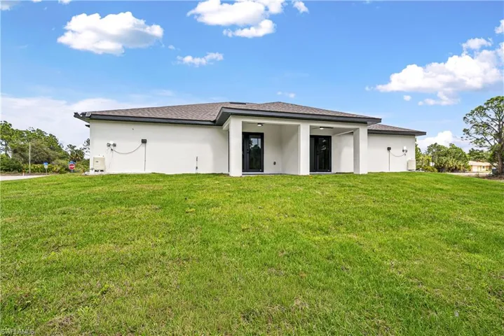 Back of house with stucco siding, a lawn, and a shingled roof