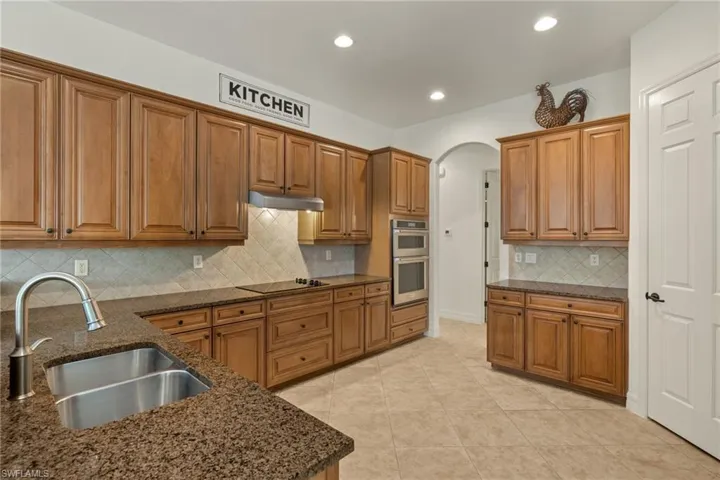 Kitchen featuring stainless steel double oven, arched walkways, brown cabinets, black electric cooktop, and recessed lighting
