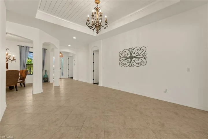 Living area with a raised ceiling, arched walkways, a chandelier, light tile patterned flooring, and recessed lighting