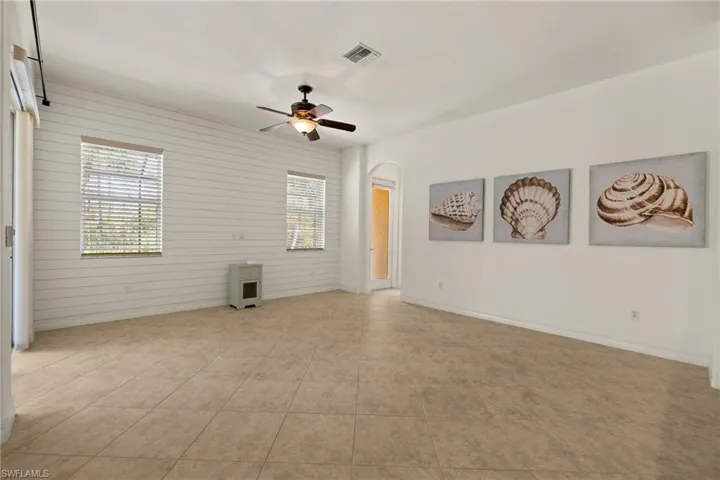 Spare room featuring a ceiling fan, arched walkways, light tile patterned floors, and wood walls