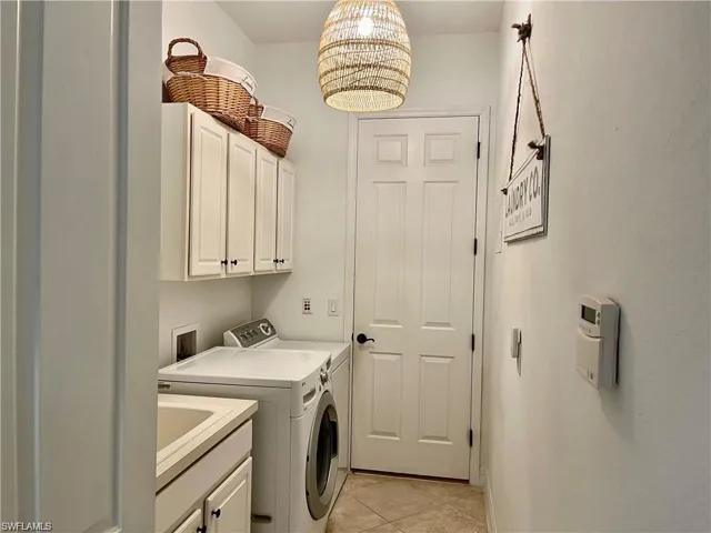 Laundry area with cabinet space, separate washer and dryer, light tile patterned floors, and a chandelier