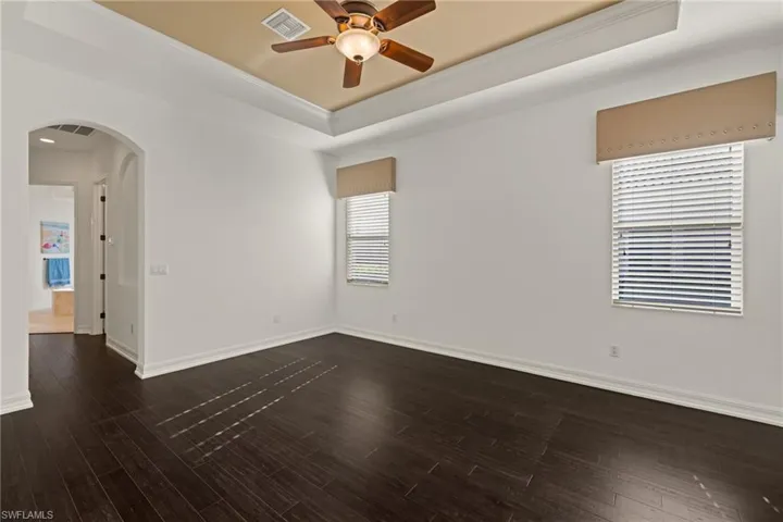 Unfurnished room with arched walkways, ceiling fan, crown molding, a tray ceiling, and dark wood-style floors