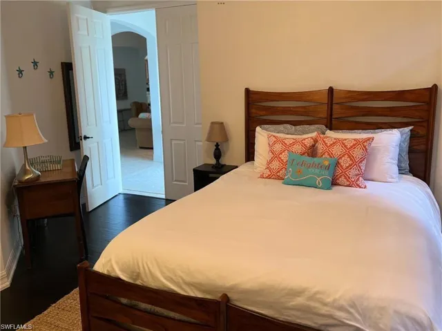 Bedroom featuring arched walkways and dark wood-style floors