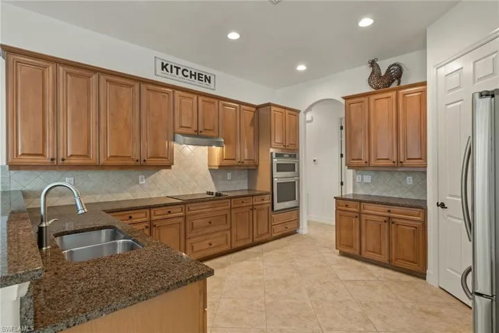 Kitchen with appliances with stainless steel finishes, arched walkways, brown cabinets, decorative backsplash, and recessed lighting