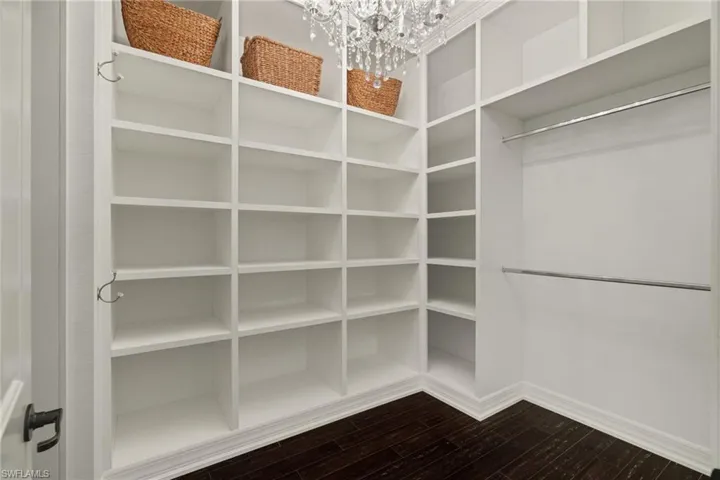 Walk in closet with dark wood-style flooring and a chandelier