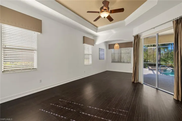 Empty room with crown molding, ceiling fan, wood-type flooring, and a tray ceiling