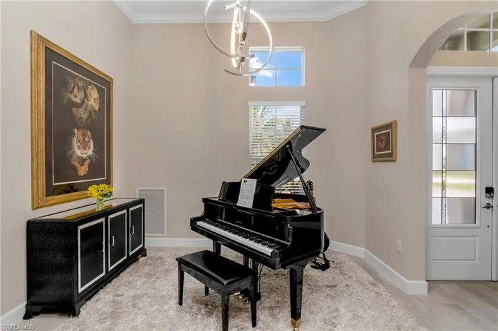 Entry foyer room is the perfect place to greet guests... used here as a music room, can also be a sitting area with bar, a gathering space with low comfy chairs, a dining room, or even an additional office! Note the stunning designer lighting chandelier, and crown molding.