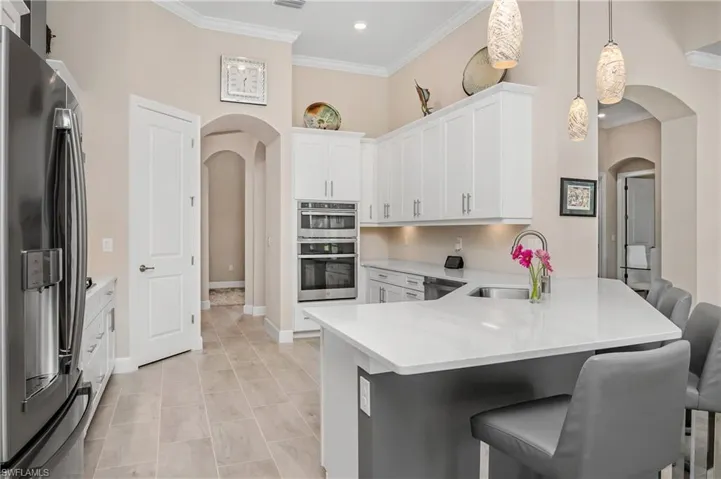 Huge kitchen features SS appliances, a large breakfast bar, high ceilings, crown molding, a walk-in pantry, and stunning designer pendant lighting.