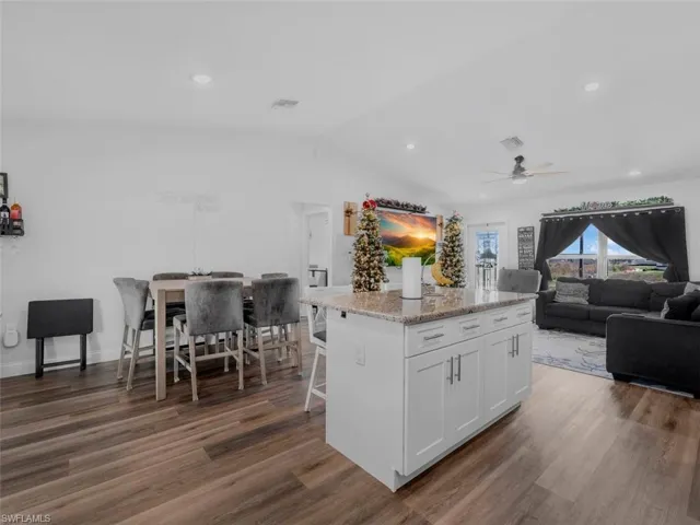 Kitchen with white cabinetry, light stone countertops, lofted ceiling, a kitchen island, and dark wood finished floors