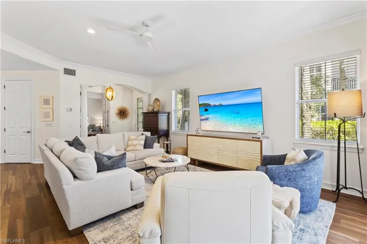 Living room featuring hardwood / wood-style floors, a ceiling fan, arched walkways, and crown molding