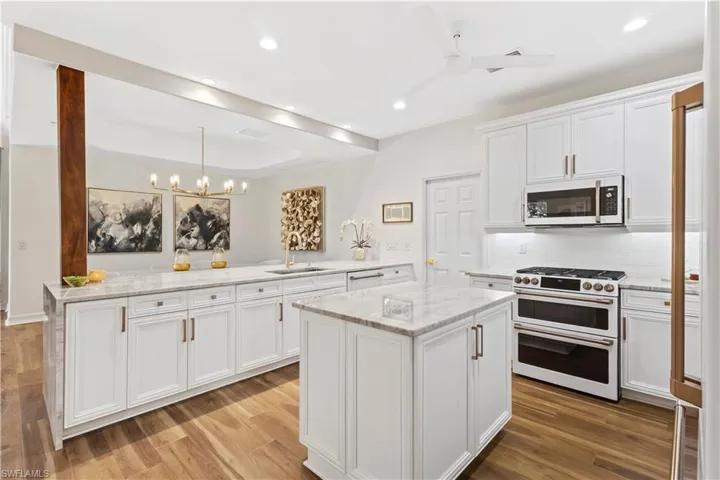 Kitchen featuring white appliances, light stone countertops, white cabinetry, a kitchen island, and a tray ceiling