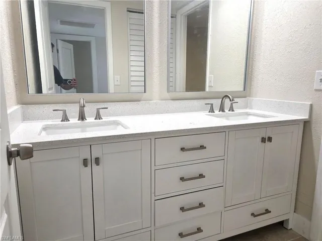 Dual vanity featuring white shaker-style cabinetry, a speckled countertop, and two undermount sinks with brushed nickel fixtures