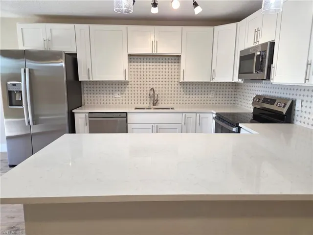 Kitchen featuring white shaker-style cabinetry, stainless steel appliances, a white patterned tile backsplash, and light-toned countertops