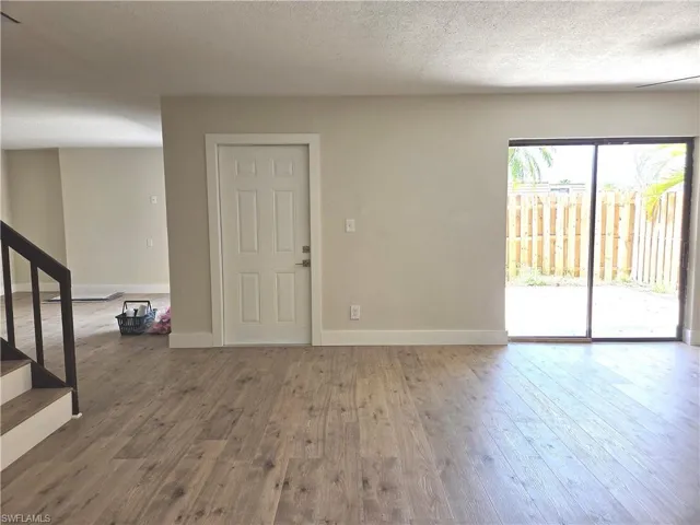 Spacious interior featuring wood-finish flooring, light-toned walls, a paneled door, and sliding glass doors opening to an exterior area with a privacy fence