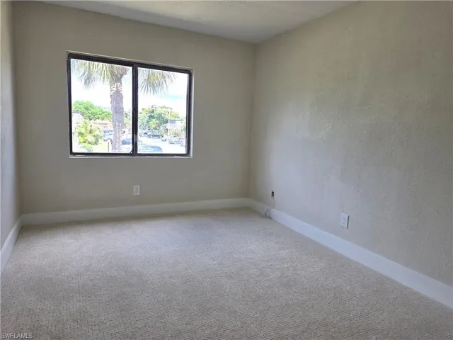 Carpeted room featuring a large window with black framing, neutral wall tones, and white baseboards