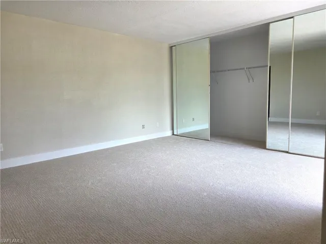 Bedroom featuring wall-to-wall carpeting, white baseboards, and a large mirrored sliding closet door