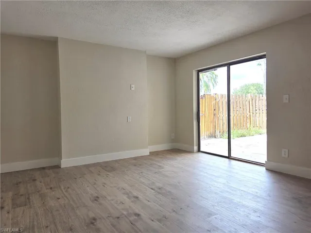 Spacious room featuring wood-finish flooring, light-toned textured walls, white baseboards, and a large sliding glass door opening to an exterior area with a wooden privacy fence