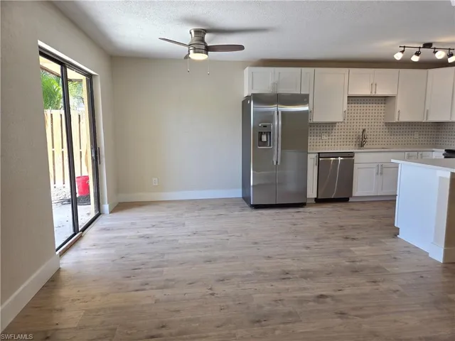Open-concept living area featuring wood-finish flooring, a contemporary kitchen, stainless steel appliances, white cabinetry, and sliding glass doors to the exterior