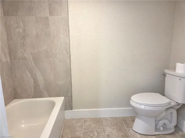 Bathroom featuring a white bathtub, floor-to-ceiling tile surround, a standard toilet, and neutral wall tones