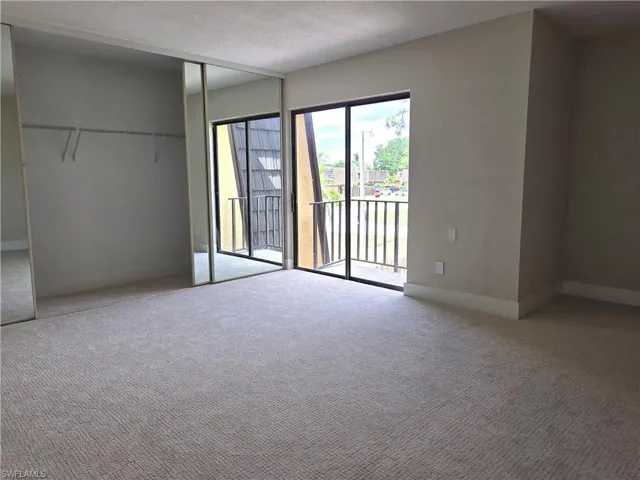 Spacious interior room featuring light-toned carpet flooring, sliding glass doors to an exterior balcony, and mirrored closet doors