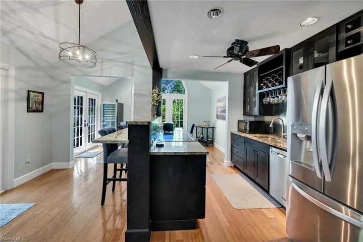 Kitchen with french doors, light stone counters, black appliances, a center island with sink, and hanging light fixtures