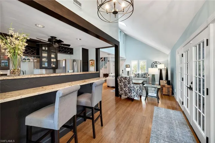 Bar with french doors, vaulted ceiling with beams, light hardwood / wood-style flooring, stainless steel refrigerator with ice dispenser, and ceiling fan with notable chandelier