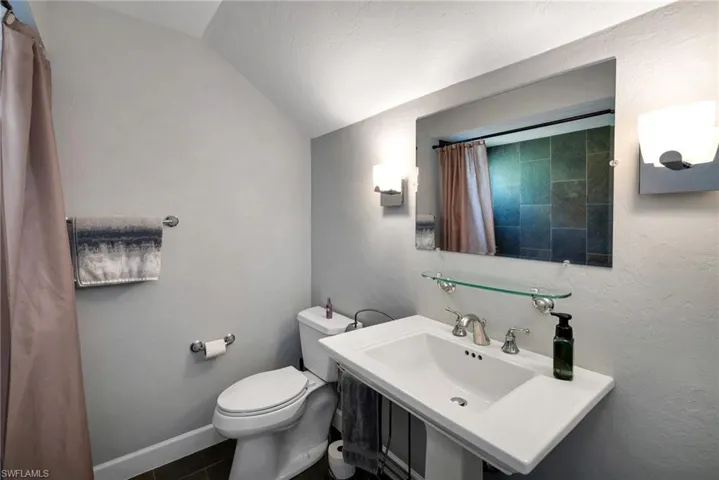 Bathroom with tile patterned flooring, toilet, lofted ceiling, and sink