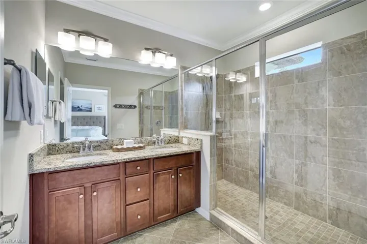 Primary Bathroom featuring tile floors, walk in shower, crown molding, double vanity with granite counter and a private water closet.
