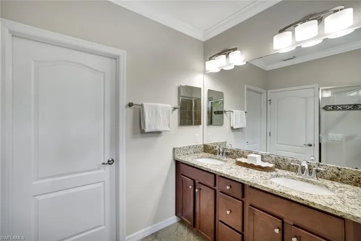 Primary Bathroom featuring tile floors, walk in shower, crown molding, double vanity with granite counter and a private water closet.