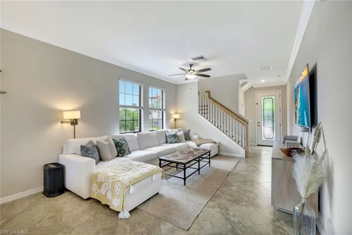 Light, bright and spacious living room featuring ceiling fan, crown molding, and tile floors.